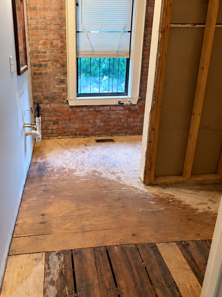 Bathroom interior after demolition, showing exposed wood flooring and wall framing